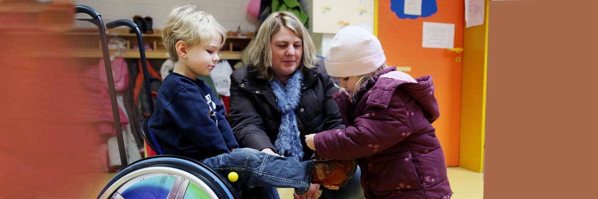 Mädchen hilft Jungem im Rollstuhl beim Schuhanziehen