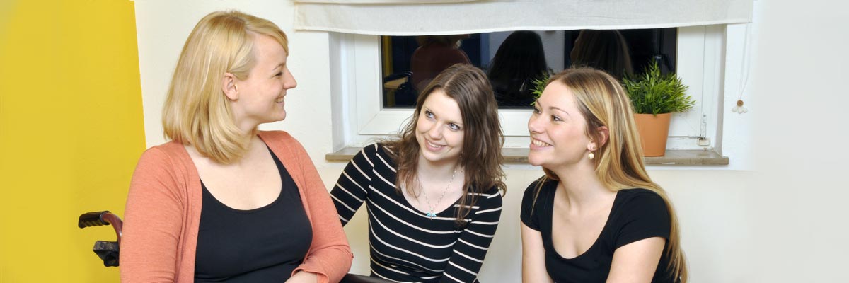Zwei junge Frauen und eine Frau im Rollstuhl.